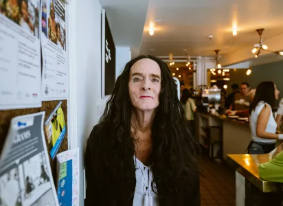 Stephanie Baughman sits indoors near a café counter, looking directly at the camera with a neutral expression.