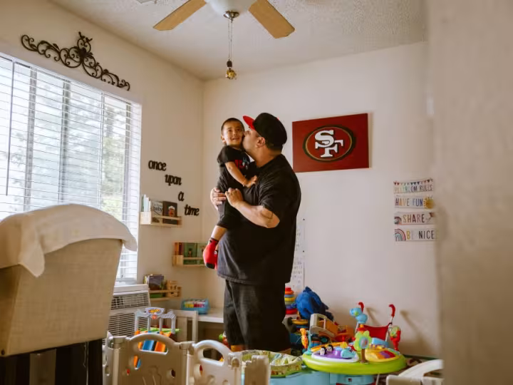 A dad kissing his son in a room full of toys.