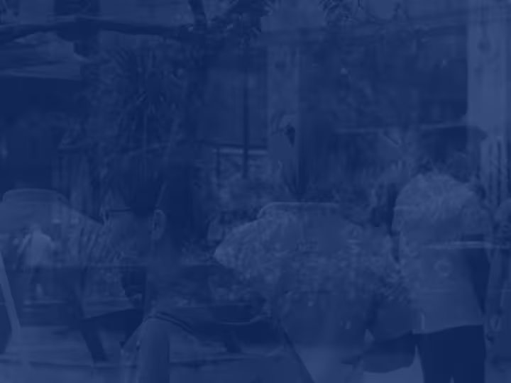 Blue-tinted photo of people walking and talking outdoors among trees and buildings.