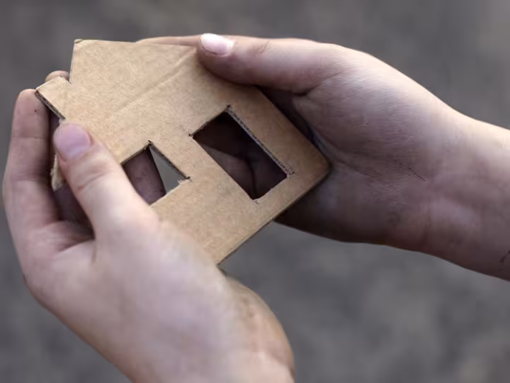 Hands handing a cardboard house.