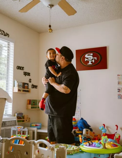 A dad kissing his son in a room full of toys.