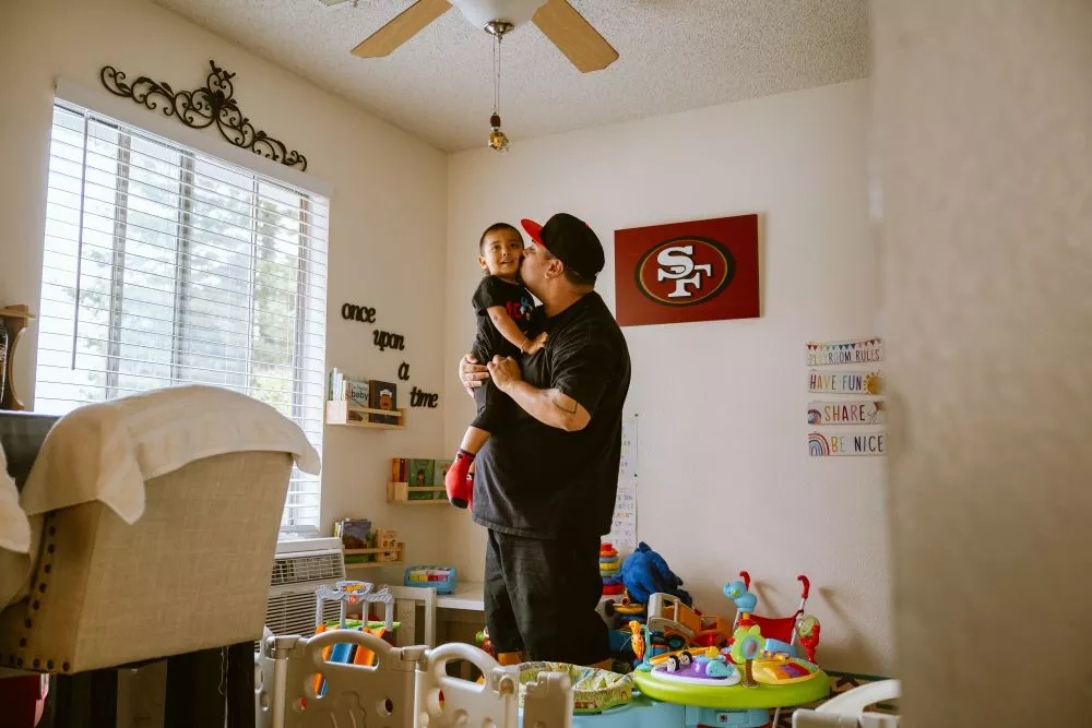 A dad kissing his son in a room full of toys.